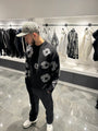 Silhouette complète présentant le pull noir et ses motifs floraux gris répartis sur l'ensemble de la maille.