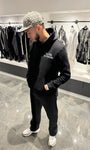 Vue de face montrant la coupe du hoodie noir, la poche kangourou et le texte blanc discret sur la poitrine.