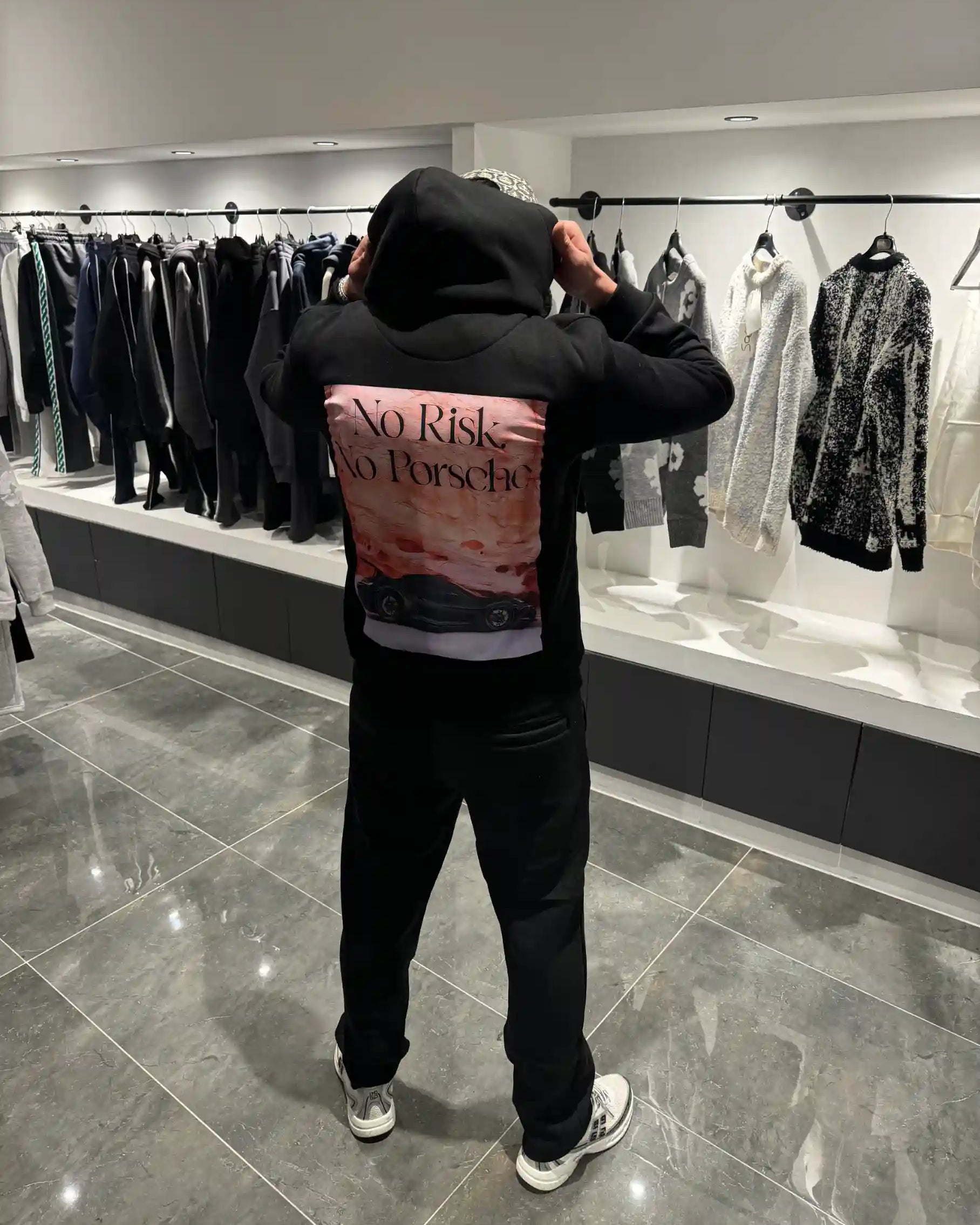 Silhouette complète de dos présentant l'impact visuel de la grande illustration verticale avec la Porsche noire sur fond rose et orange.