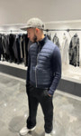 Silhouette complète présentant la veste hybride bleu foncé, mettant en valeur le contraste de texture entre le jersey et le matelassage.