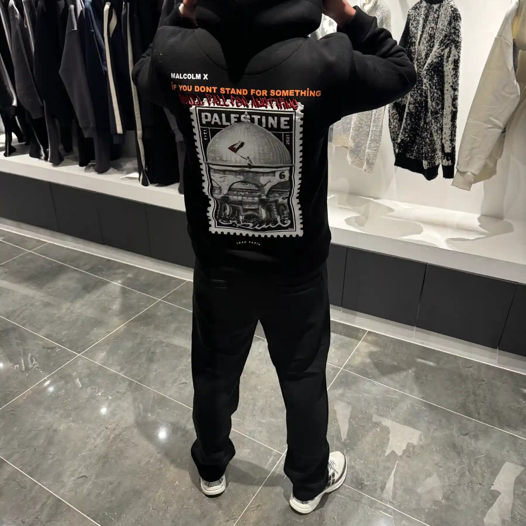 Silhouette complète de dos présentant le hoodie noir oversize avec la grande photo de la Palestine et l'écriture arabe.