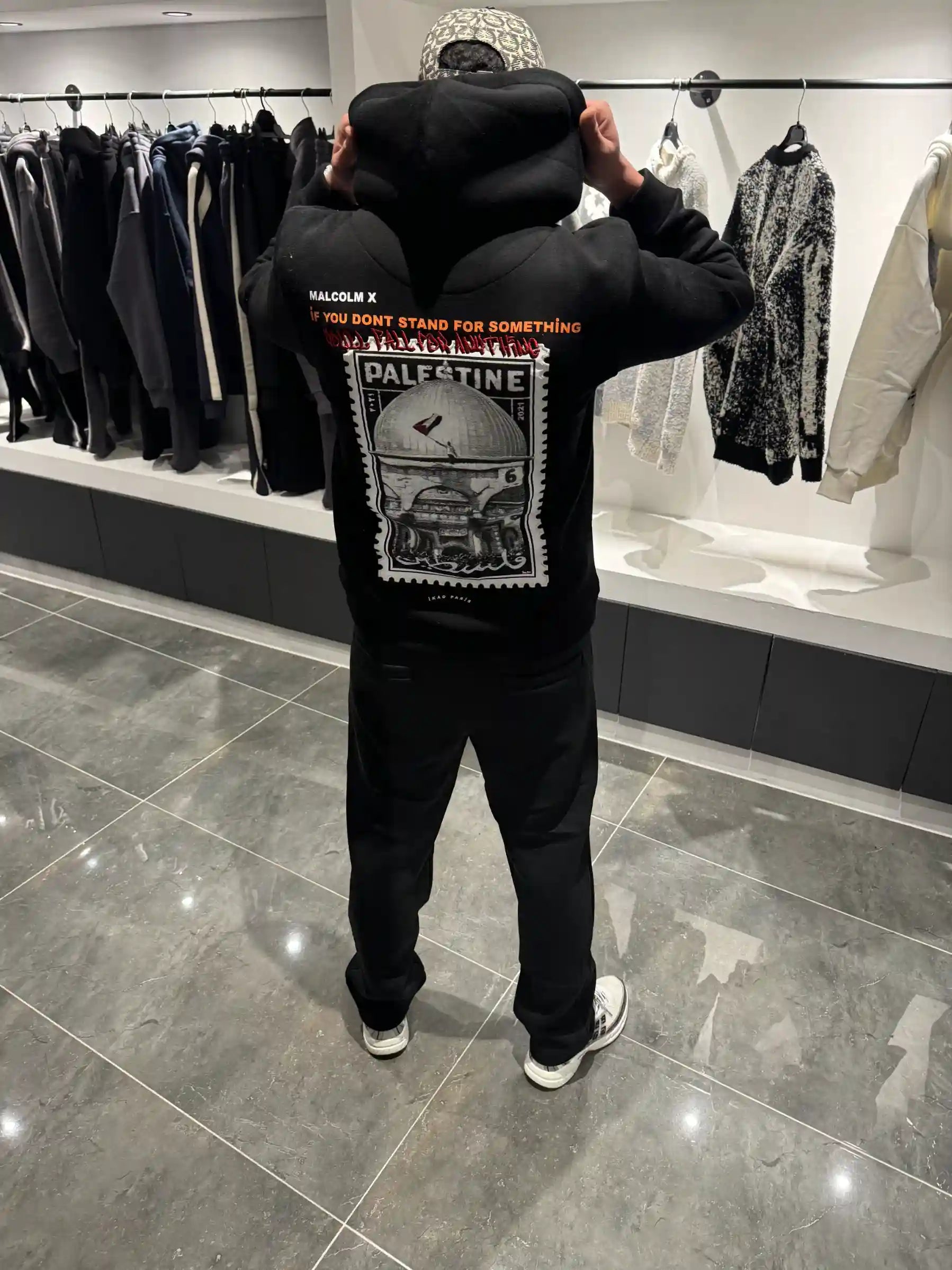 Silhouette complète de dos présentant le hoodie noir oversize avec la grande photo de la Palestine et l'écriture arabe.