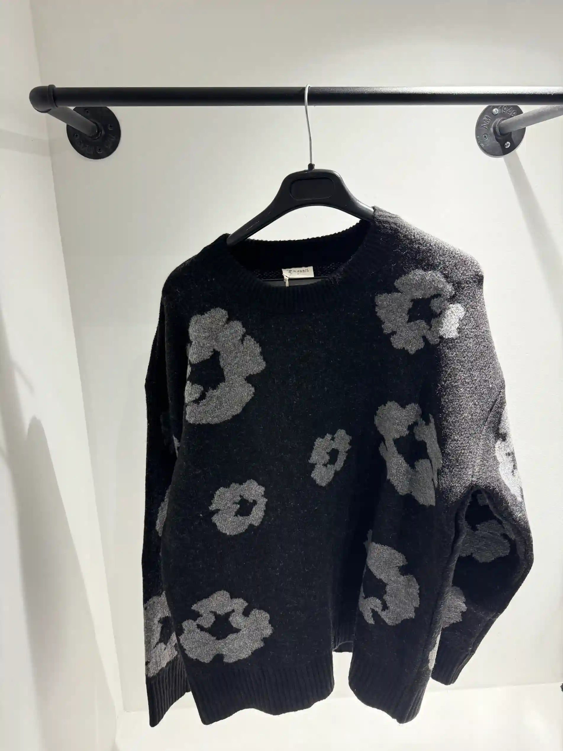 Présentation du pull noir sur cintre, illustrant le tombé fluide et la répartition des motifs floraux.