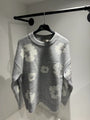 Présentation du pull gris sur cintre, illustrant la qualité du tissage et le design floral all-over.