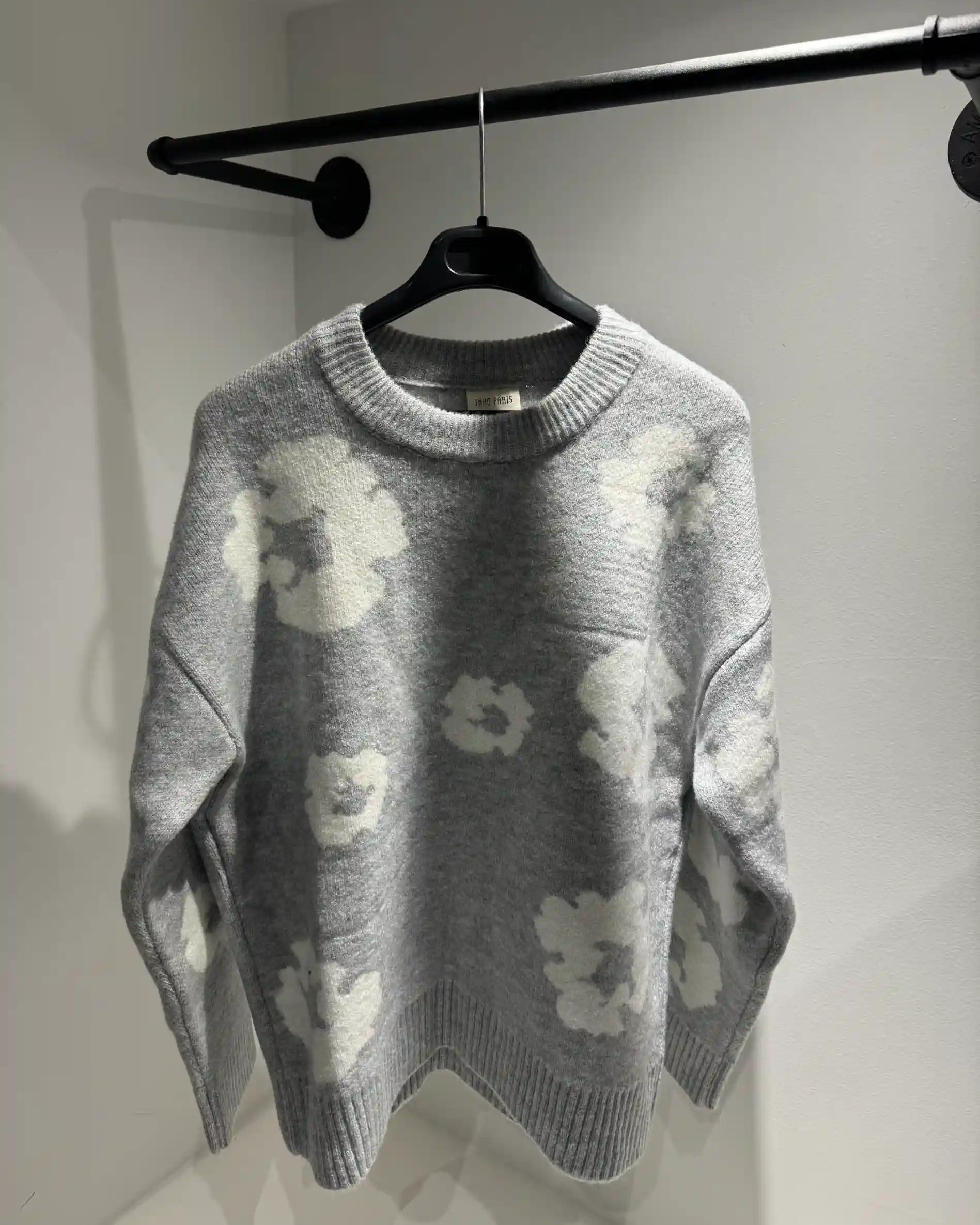 Présentation du pull gris sur cintre, illustrant la qualité du tissage et le design floral all-over.