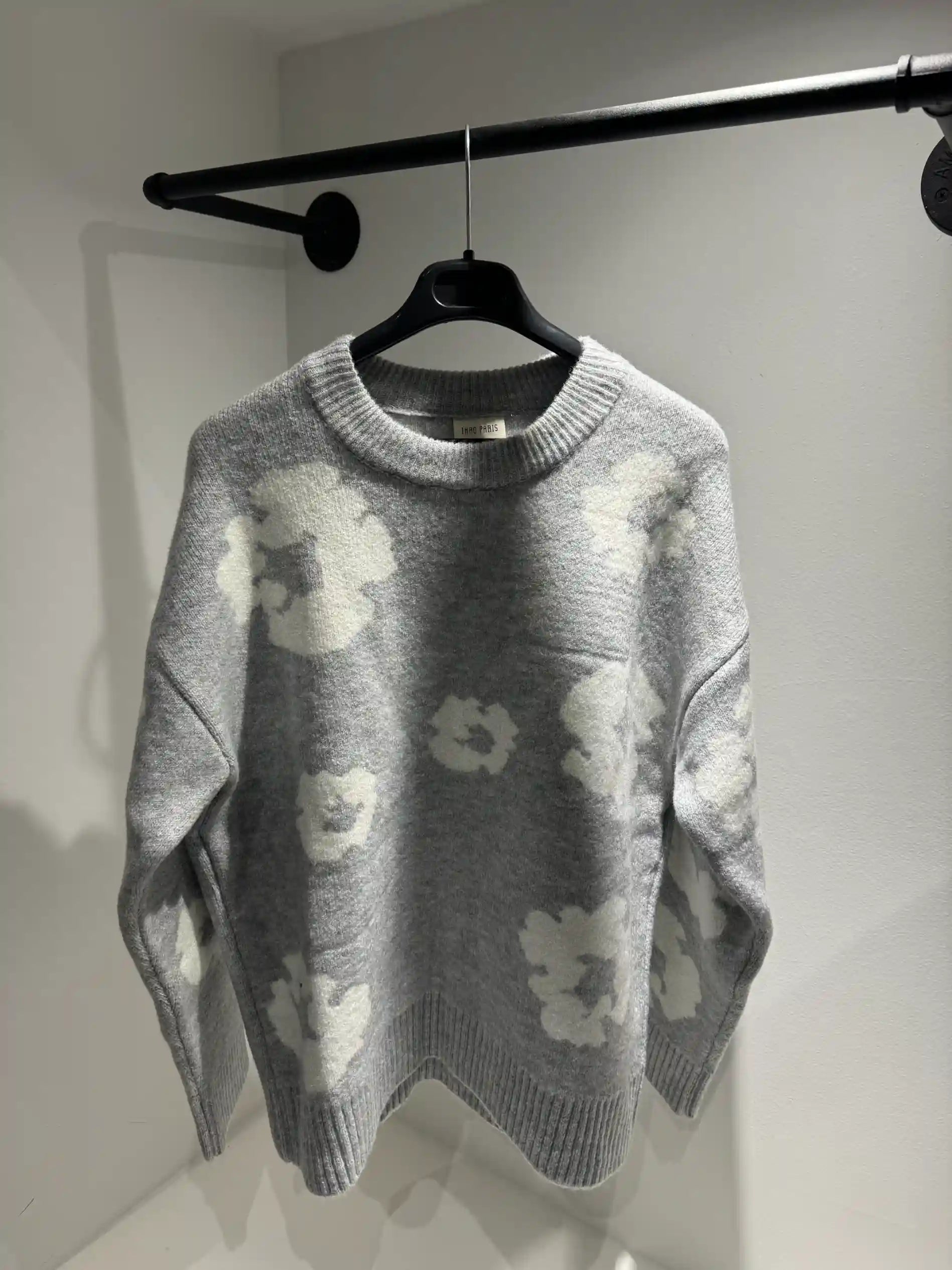 Présentation du pull gris sur cintre, illustrant la qualité du tissage et le design floral all-over.