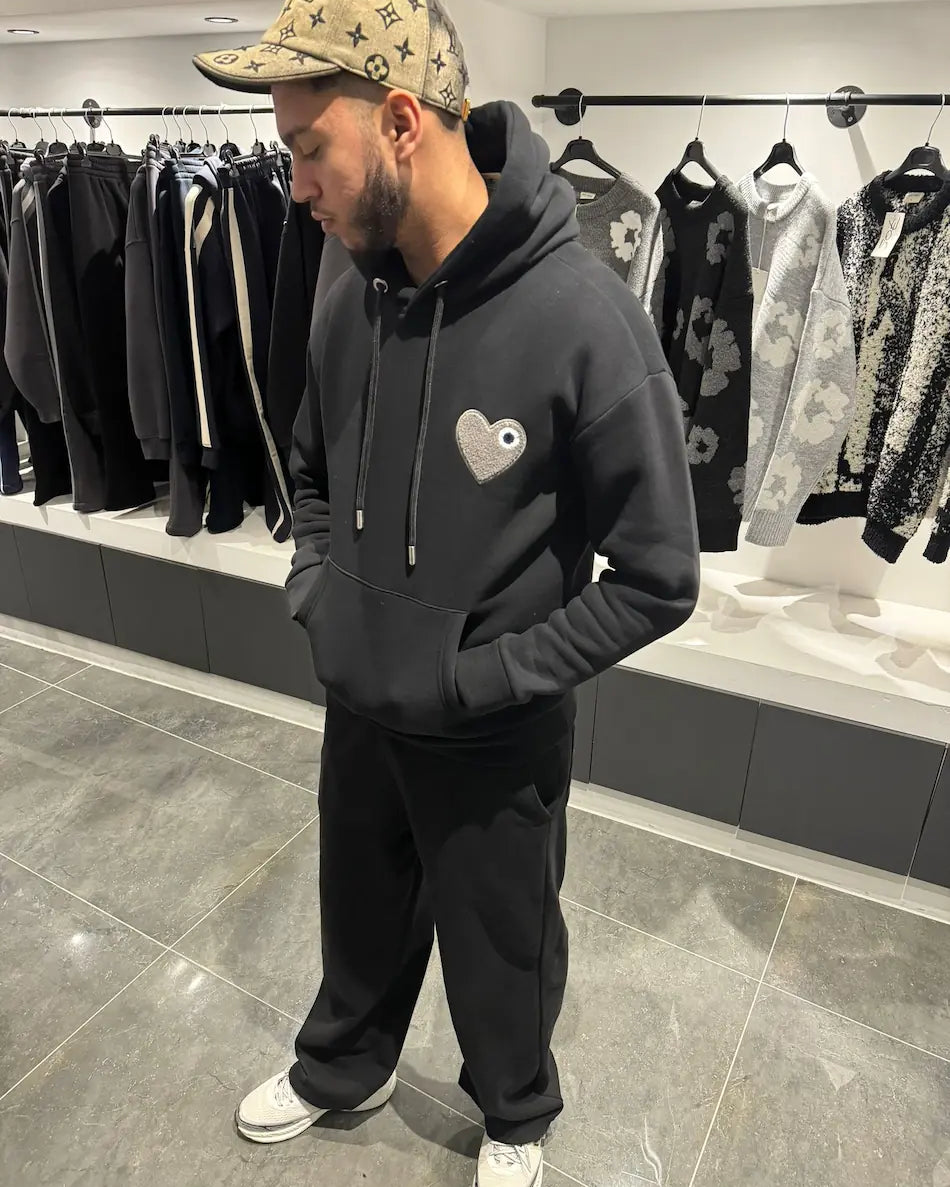 Hoodie noir premium présentant le logo cœur gris en matière éponge brodé en relief sur la poitrine.
