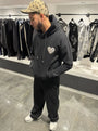 Hoodie noir premium présentant le logo cœur gris en matière éponge brodé en relief sur la poitrine.