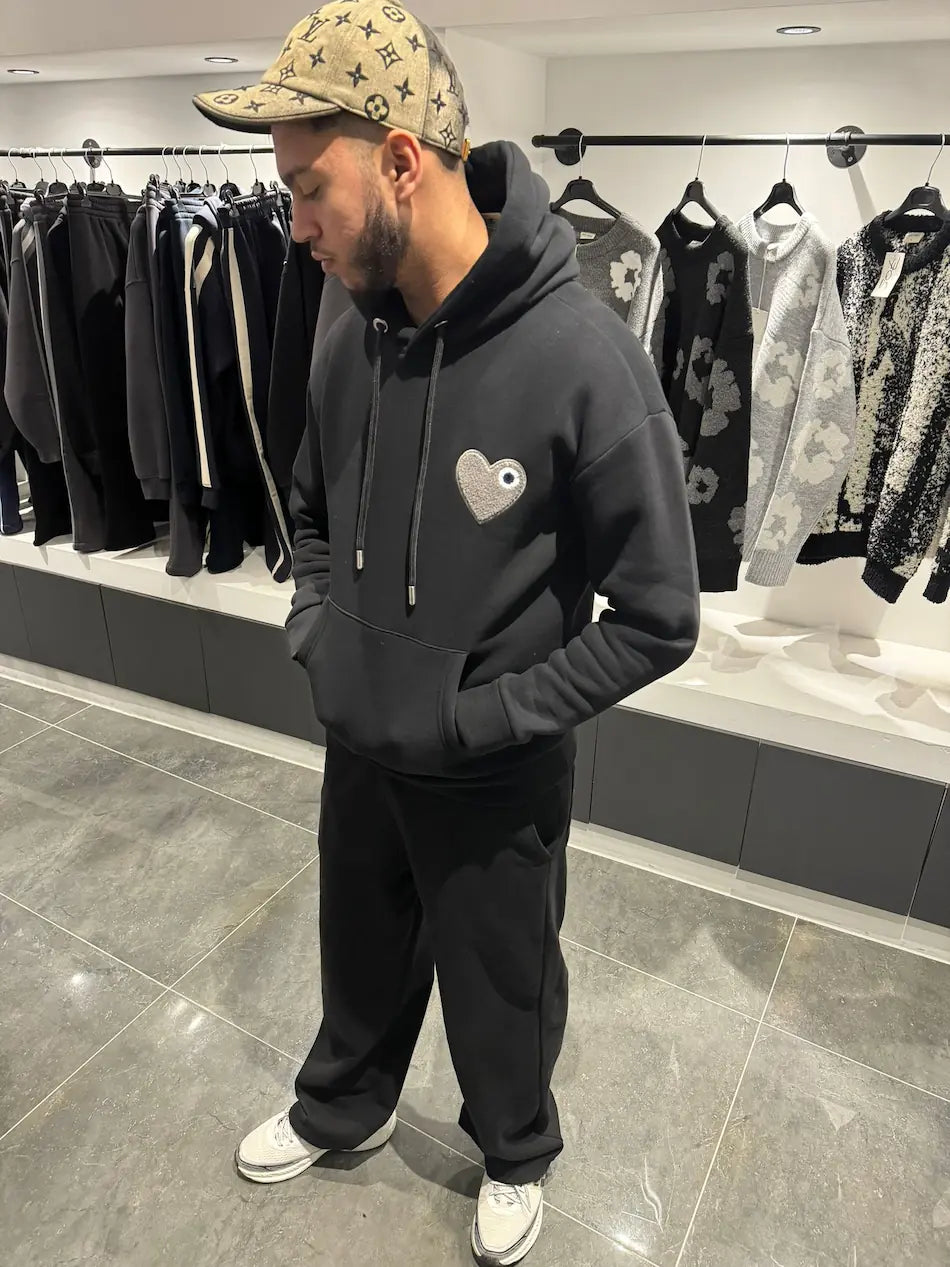 Hoodie noir premium présentant le logo cœur gris en matière éponge brodé en relief sur la poitrine.